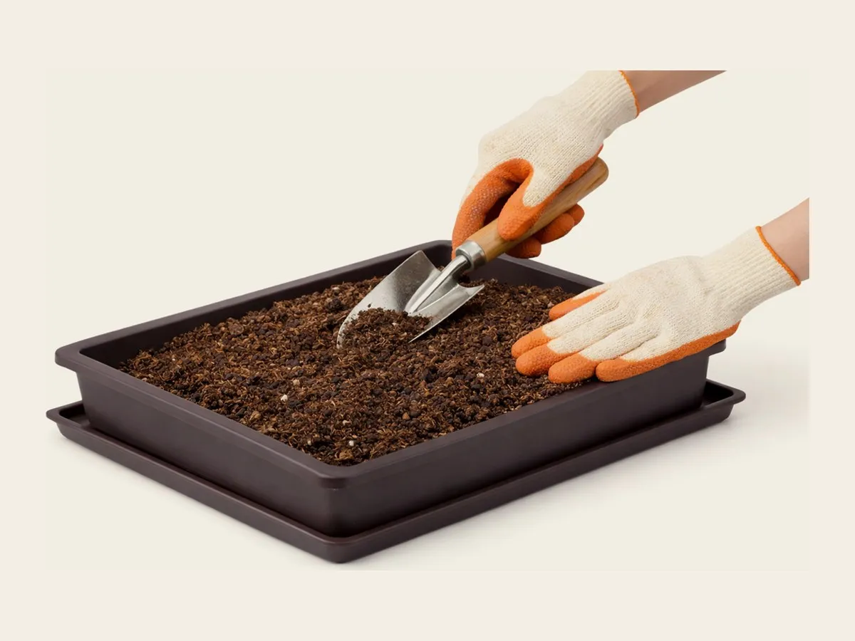 Gloved hands fluffing fully expanded coconut coir in a tray with a small garden trowel